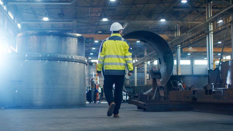 Man with a yellow reflecting security vest walking through a factory hall