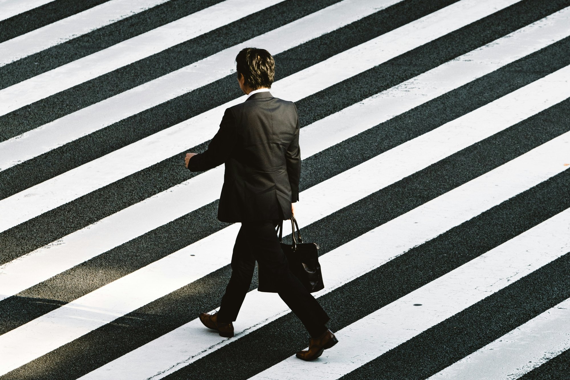 A person in a suit walks across a zebra