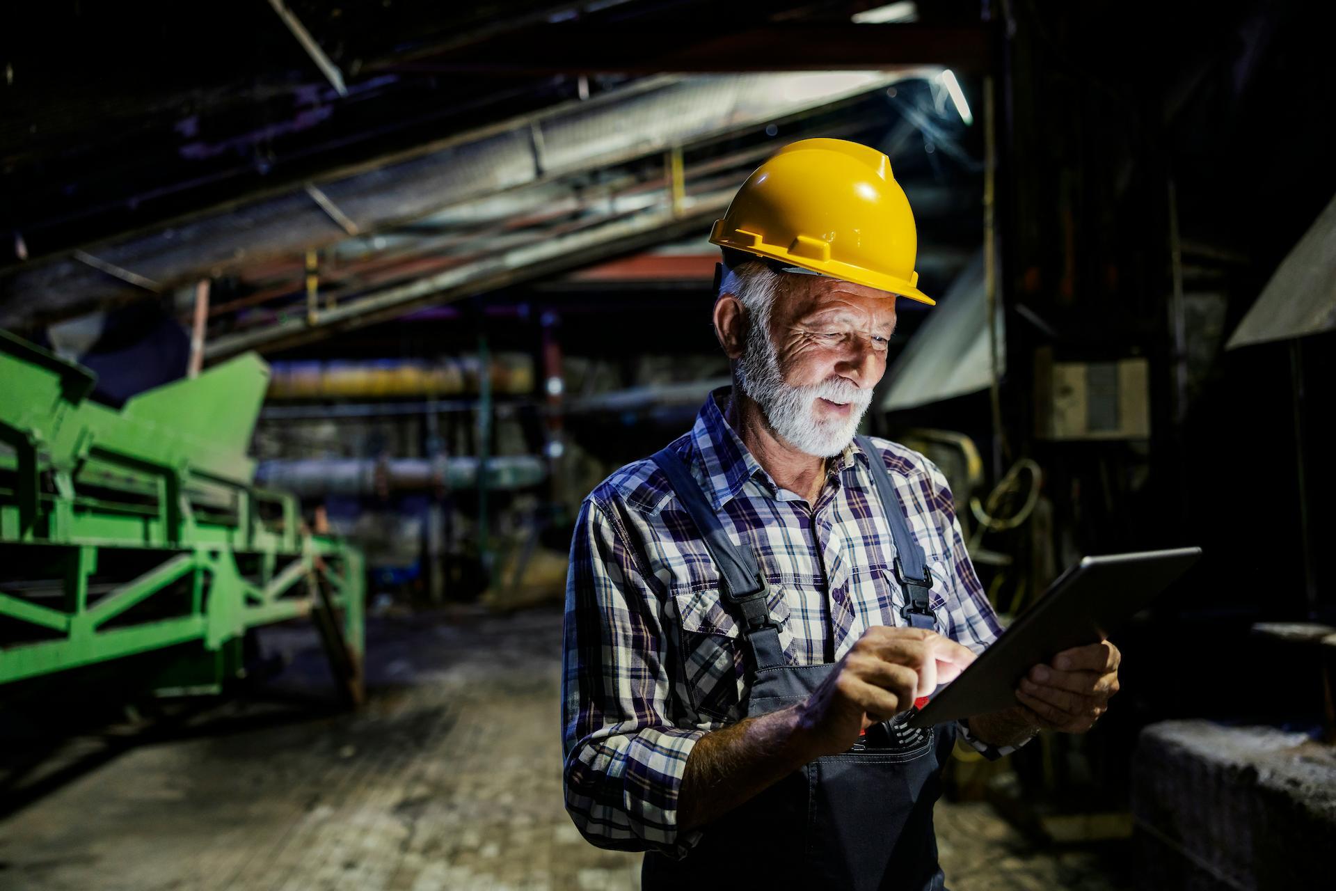 Older man working in factory holding a tablet