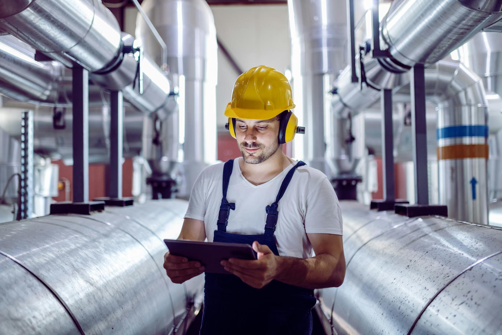 man wearing yellow hard hat in factory and looking at tablet