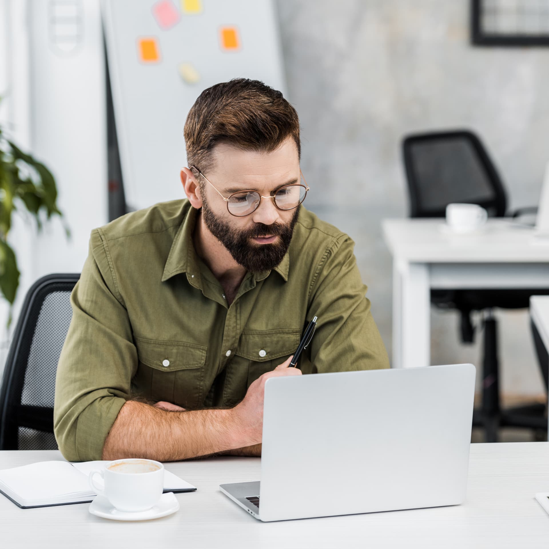 Man with a beard and glasses intently working on a laptop at an office desk
