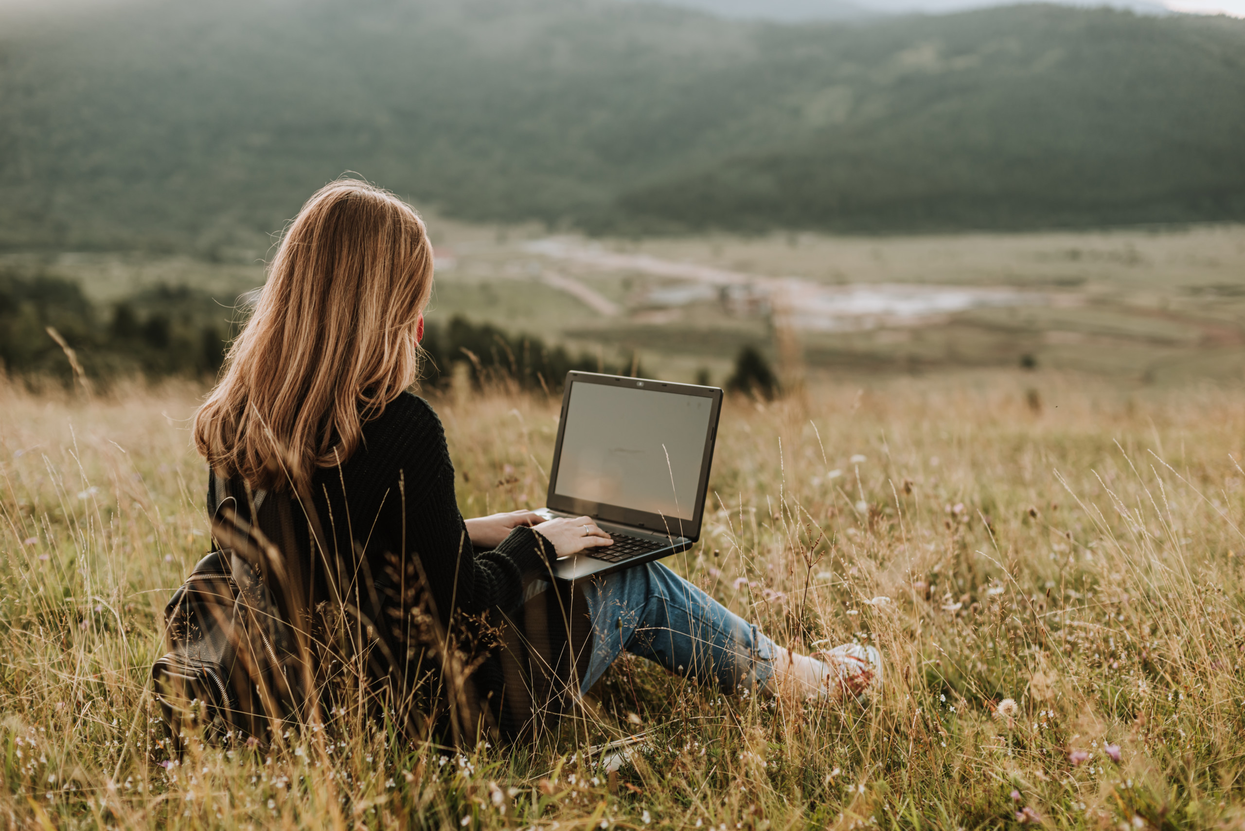 Frau mit Laptop sitz auf einem Feld