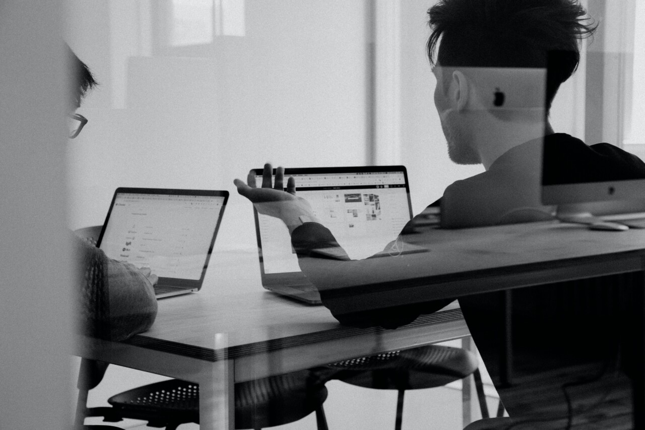 Man and a woman in an office with laptops searching for information and discussing