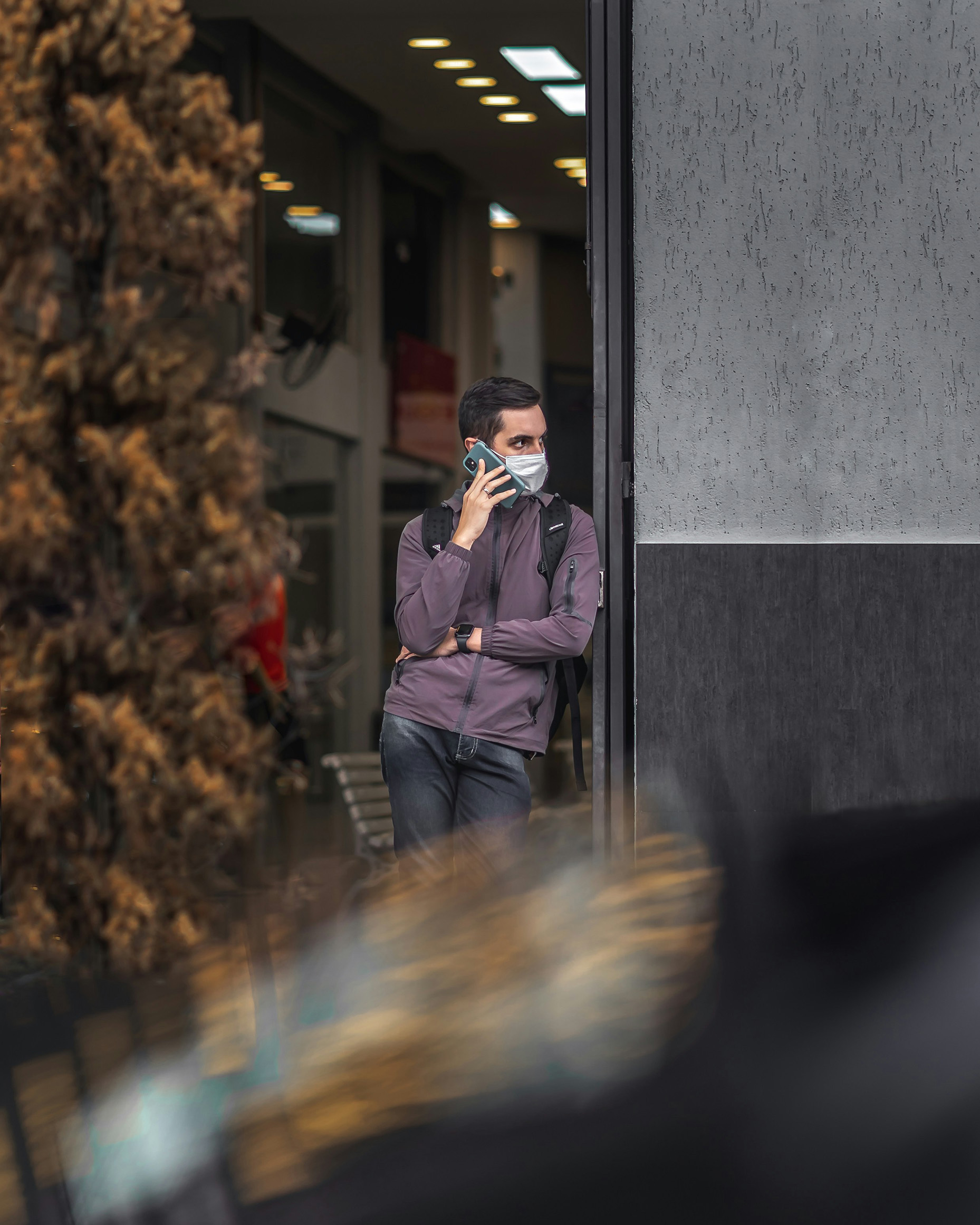 Young man speaking with a phone on a street, wearing mask